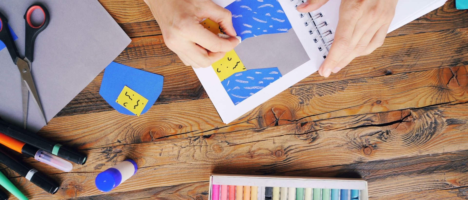 Manos recortando papeles de colores para una manualidad sobre una mesa de madera