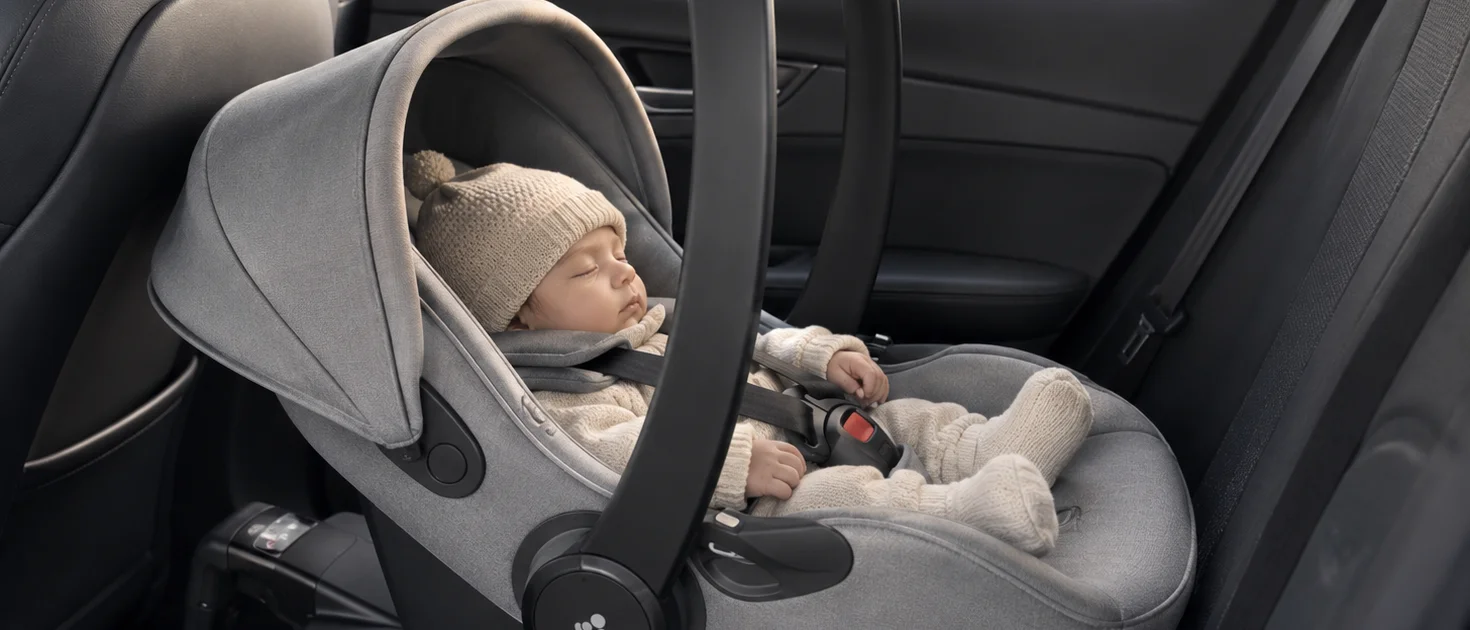 Bebé recién nacido dormido en una silla de coche Grupo 0, instalada en el asiento trasero del vehículo