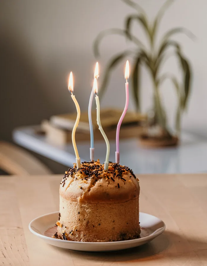 Tarta pequeña con velas de colores encendidas sobre una mesa de madera