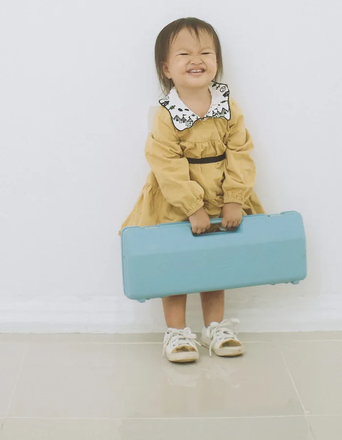 Niña pequeña sonriendo con una maleta turquesa
